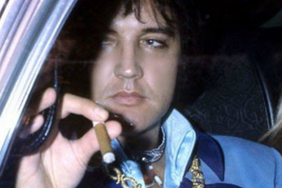 Elvis Presley sitting in a car, holding a cigar