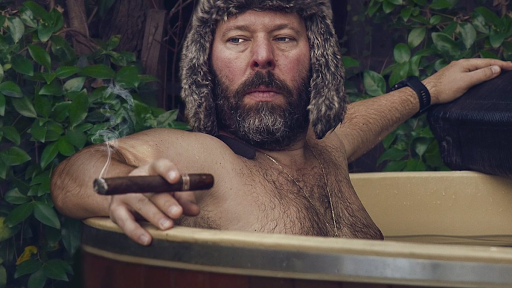 Bert Kreischer in a hot tub holding a cigar in hand