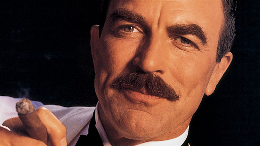 Tom Selleck holding a cigar with a confident smile