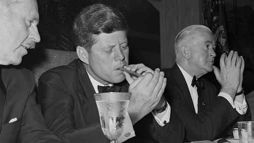 John F. Kennedy lighting a cigar at a formal event